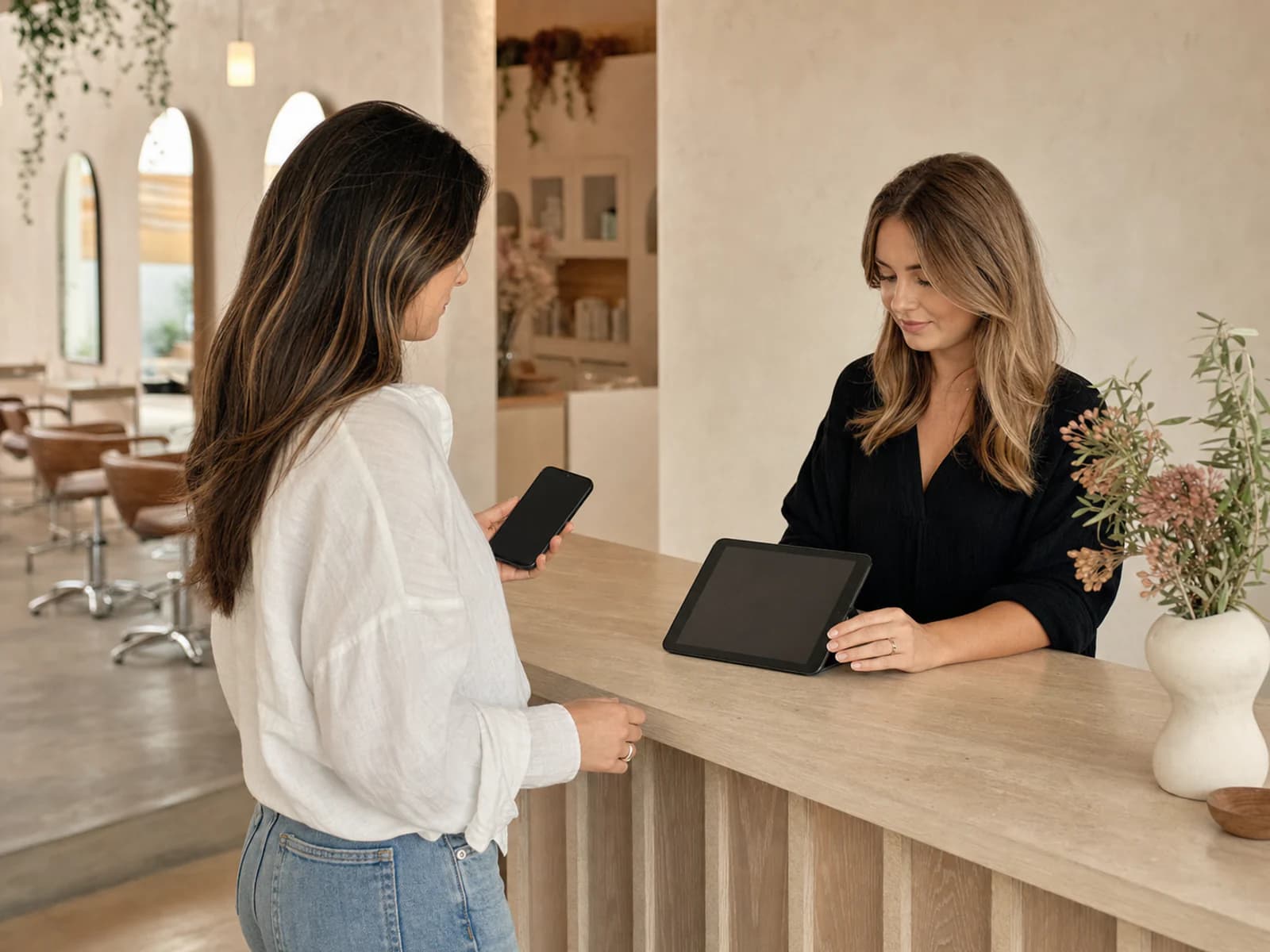 Salon receptionist and client using a tablet and phone at the front desk