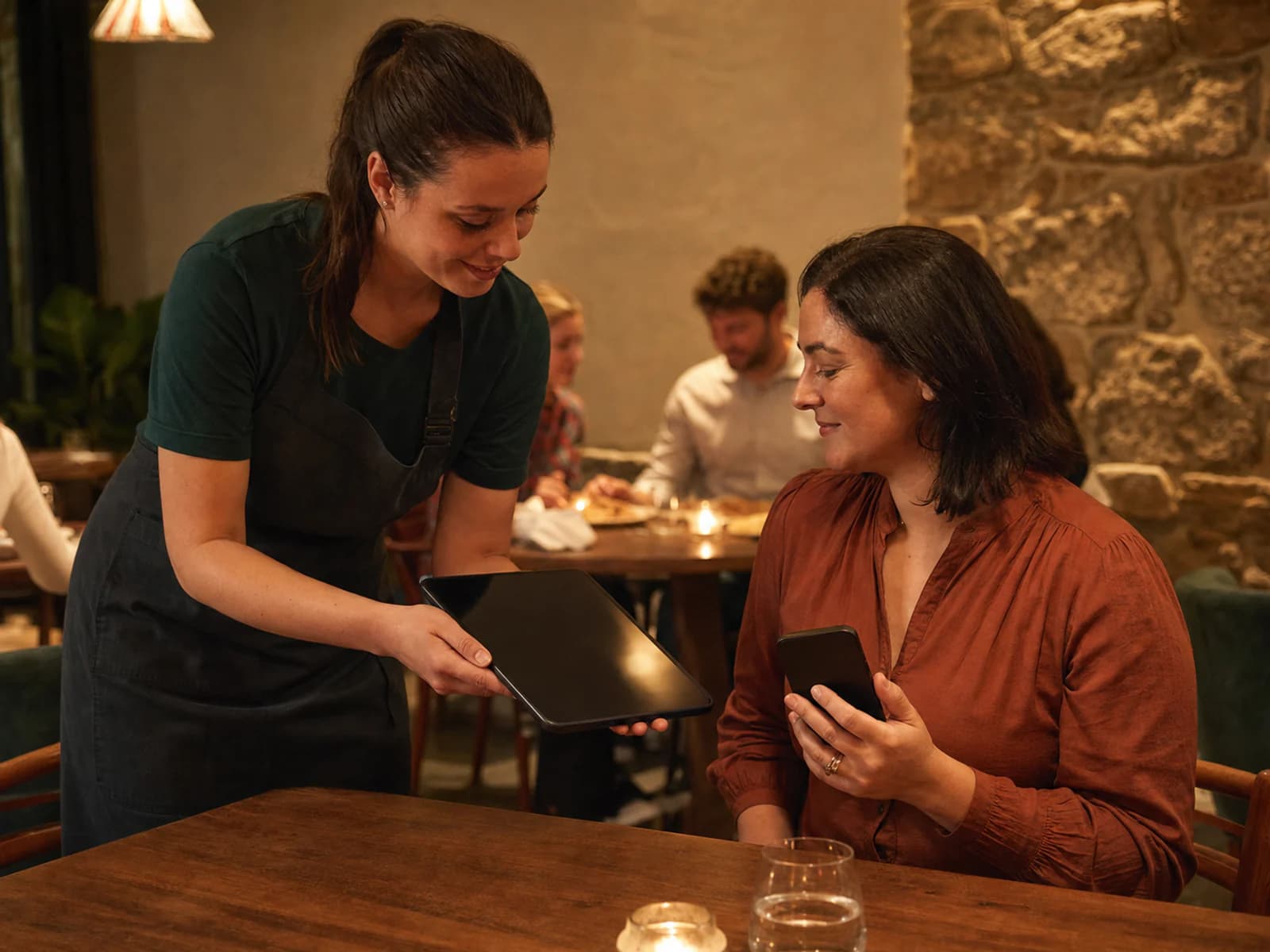 Restaurant staff member and guest using a tablet and phone at the table